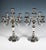 Two elegant five-candle holders on a stepped, curved base with four triple-pleated curving pleats that continue up the...