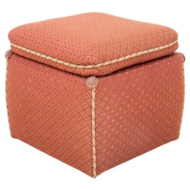 A square ottoman or footstool with a square pillow on top with rope edges and gathered corners. Covered in fabric rose...