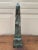 A beautifully proportioned marble obelisk in richly veined shades of black, brown, and gray. The sculptural silhouette and...