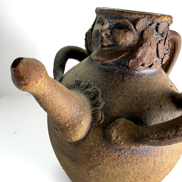 Expressive ceramic pitcher by Louis Mendez, featuring a sculpted bearded face, applied arms, a rounded body, and a curved...