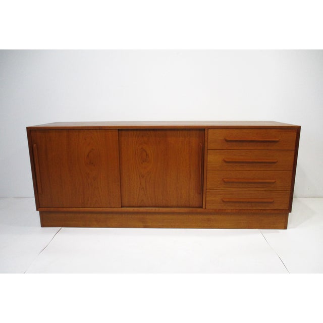 A Mid Century teak credenza or sideboard with double sliding doors having storage and adjustable shelves. To the other...