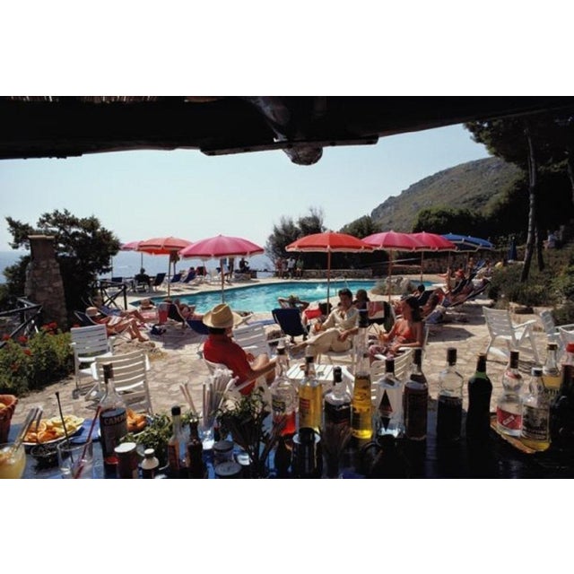 Poolside Bar by Slim Aarons Guests seen from a poolside bar at the Hotel Il Pellicano in Porto Ercole, Italy, August 1980....
