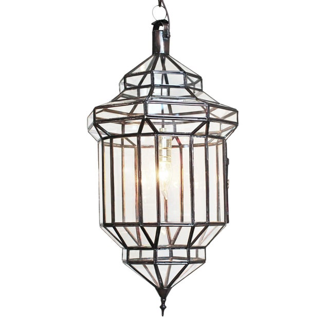 Striking Moroccan pendant lantern hand crafted from clear glass panels set within a dark bronze finish metal frame....