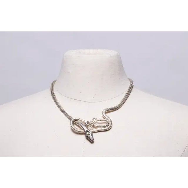 A condensed herringbone pattern snake chain necklace with a coiled snake at the front with faceted garnet eyes and a...