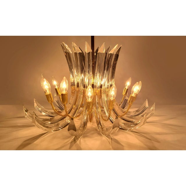 Bent brass sleeves act as 12 torches of light with sweeping crystal prisms; curving to reflect colors of pink, blue,...