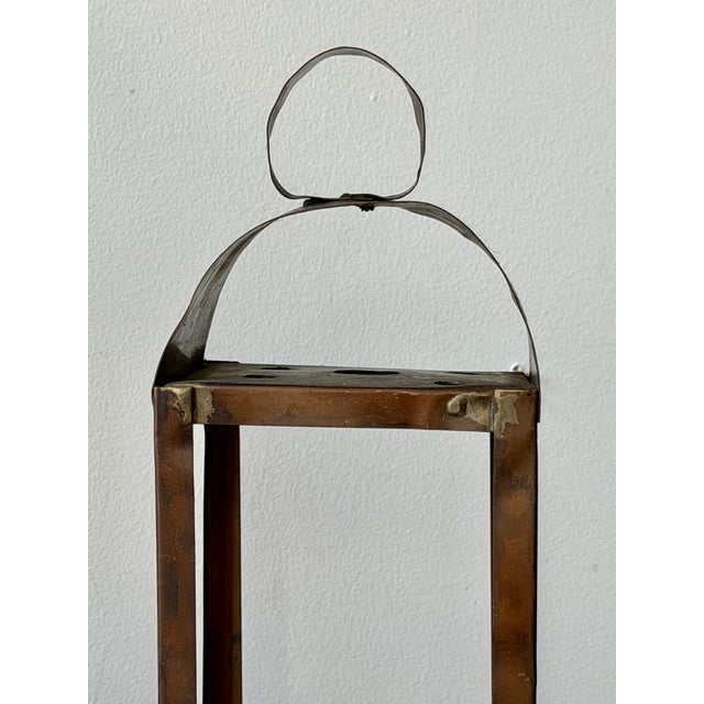 This antique handcrafted copper lantern features a simple open-frame design with a curved hood, loop handle, and rich aged...
