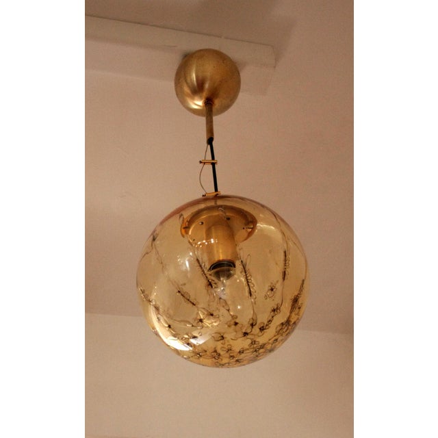 An Italian designed Murano glass sphere pendant with brass hardware by La Murrina. Brass inserts in the blown...