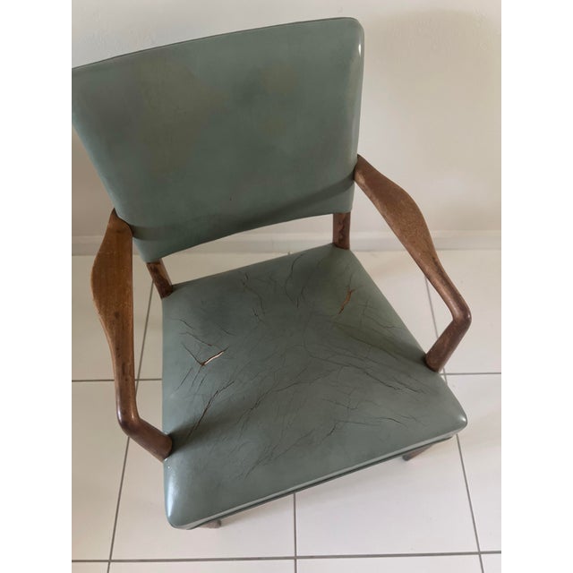 Vintage armchair is constructed with a solid wood frame and sage green vinyl upholstery. The piece has sculpted wooden...