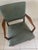 Vintage armchair is constructed with a solid wood frame and sage green vinyl upholstery. The piece has sculpted wooden...