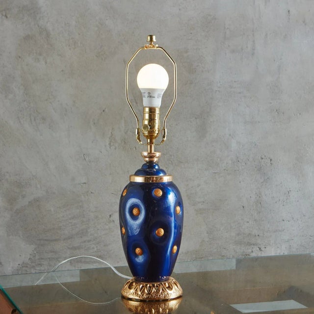 A vintage Italian table lamp with a striking royal blue glazed porcelain body and gold metal medallion detailing. It...