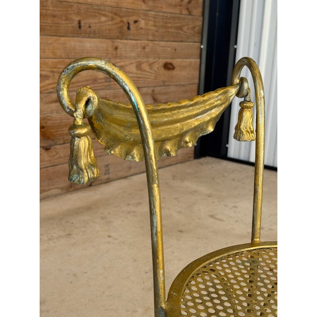 A striking vintage Hollywood Regency gilt metal vanity chair featuring an elegant swag back design accented with...