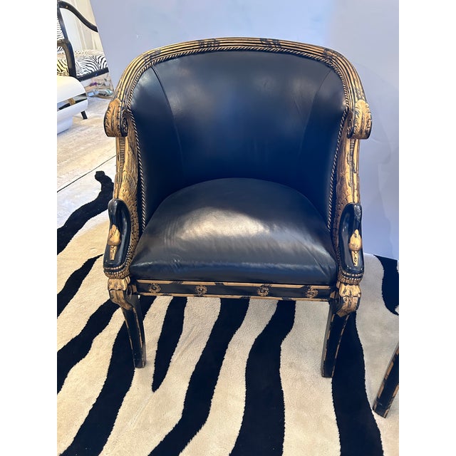 Impressive pair of Empire style black and gilded wood club chairs having black leather upholstery, curved backs and arms...