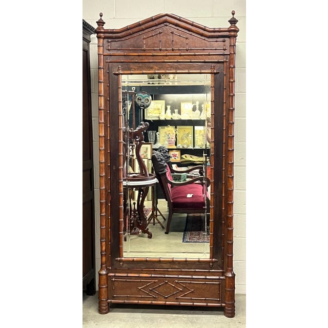 Late 19th-century Victorian faux bamboo armoire featuring a full-length mirrored door, turned finials, and a wide bottom...