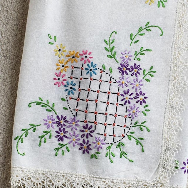 A pretty and colorful mid-century hand-embroidered tablecloth. The piece is square and created from linen. Crotcheted lace...