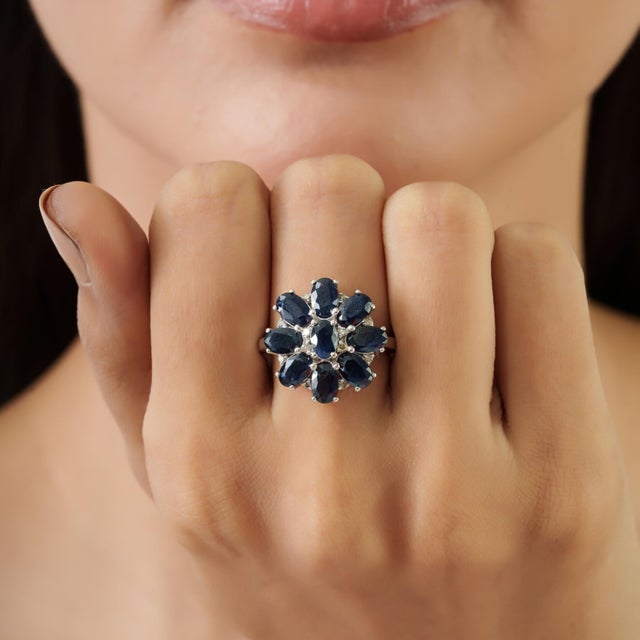 5.06 ct. of blue sapphires are arranged in a floral cluster, with nine oval-cut gemstones forming a balanced petal-like...