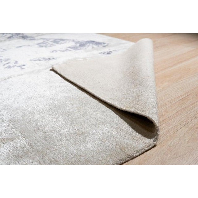 This hand knotted pile rug is crafted from viscose and features a primary color palette of ivory, beige, cream, and white....