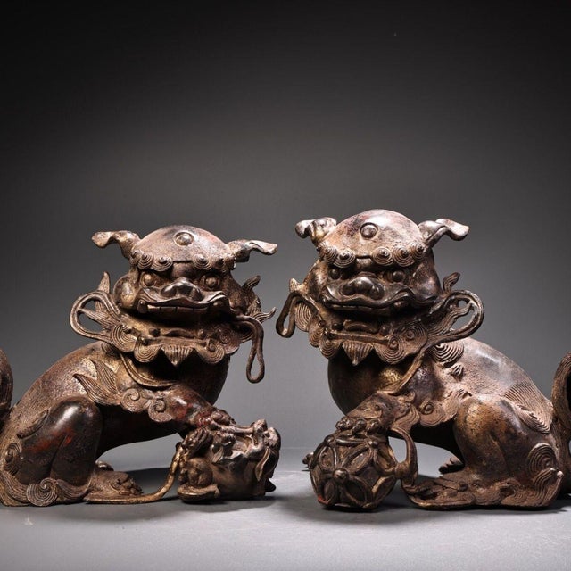 This is a matching pair of cast bronze guardian lion (Foo Dog) figurines, featuring a gilded finish with a dark, aged...