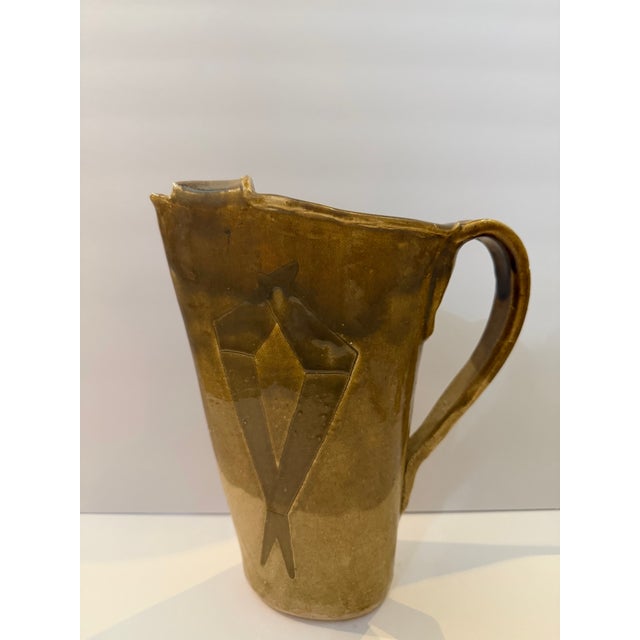 Handcrafted studio pottery ceramic pitcher featuring geometric carved decoration and earthy brown and sand-toned glaze....