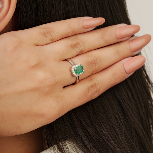 This elegant silver ring showcases a rectangular-cut emerald weighing approximately 0.56 carats total weight, framed by a...