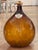 A blown amber glass demijohn with a shield reading "Clos du Roy." Cork stopper with burlap collar.
