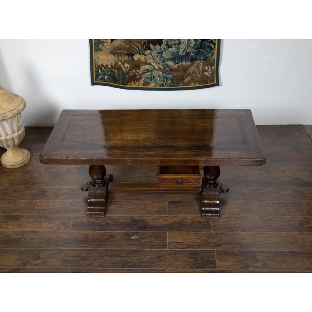 An Italian walnut table from the 19th century, with trestle base, turned legs, cross stretcher and single drawer. Created...
