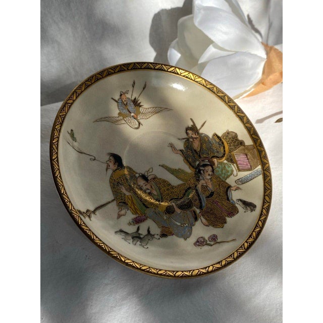 This finely detailed Japanese plate features a narrative scene of four robed figures gathered beneath a flying immortal,...