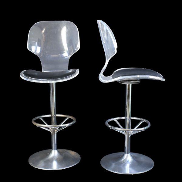 A pair of lucite and chrome bar stools for Hill Manufacturing, with clear acrylic frames and gleaming chrome accents. The...