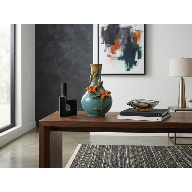This striking ceramic vase features a bulbous body that tapers into a slender neck, beautifully finished in a glossy teal...