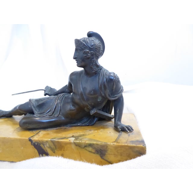 This bronze figure of a reclining Greek warrior is mounted on a rectangle of Siena yellow marble.