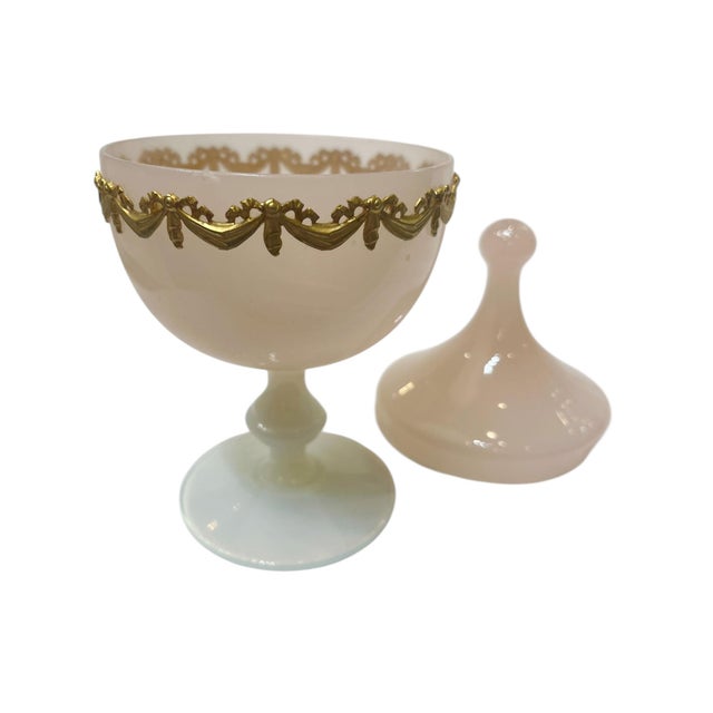 A charming vintage French opaline glass covered box in a soft blush pink tone, raised on a classic white pedestal base....
