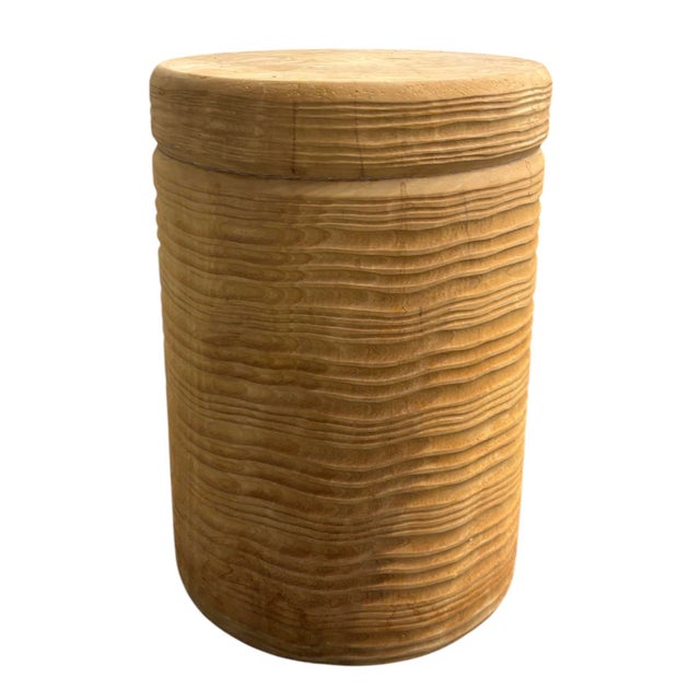 Unmarked round wood side table with a carved, ridged texture and a hollow interior, in a natural blonde finish.