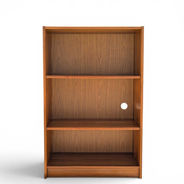 A petite vintage teak bookcase with warm grain, clean lines, and open shelving. Its shallow depth and compact scale make...