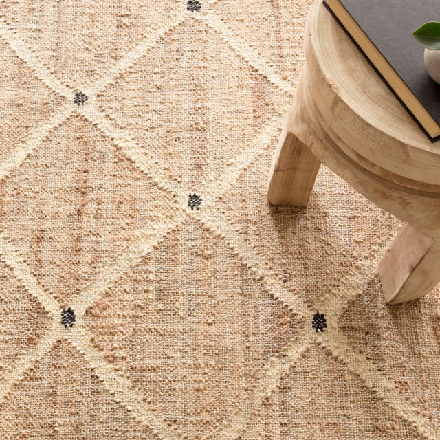 A large ivory latticework pattern emerges from the relaxed natural jute kilim weave foundation with a punctuating charcoal...