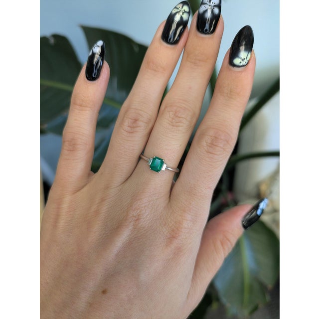 A Colombian emerald in a vivid, slightly bluish green sits at the heart of this solid 14K white gold ring, flanked by two...