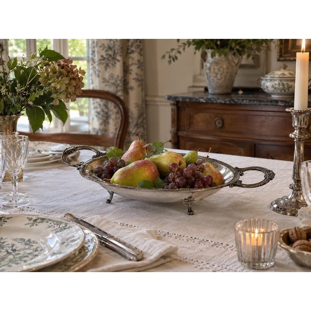 An elegant antique oval centerpiece platter in silver-plated metal, featuring ornate openwork handles, shell-shaped...