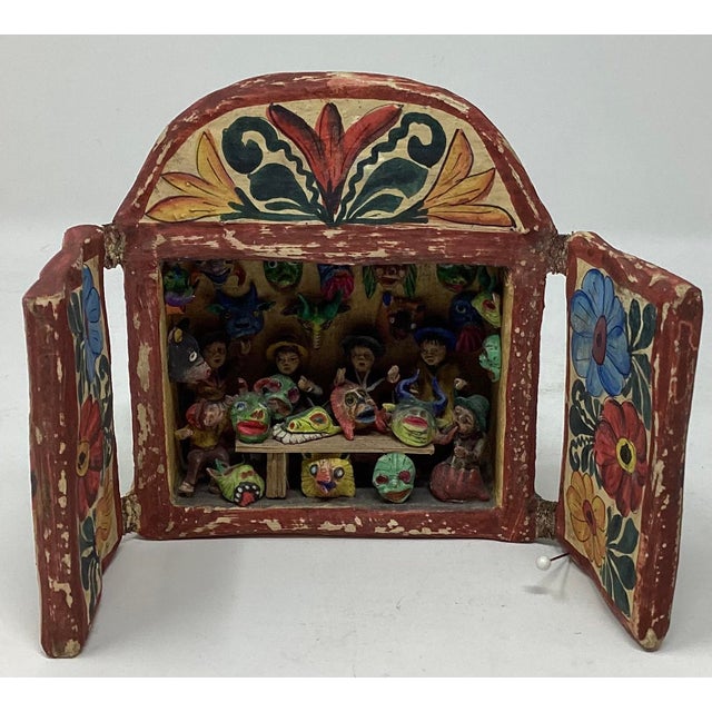 This folk art diorama features a mask store or workshop. The colorful figures and masks are typically crafted from a...