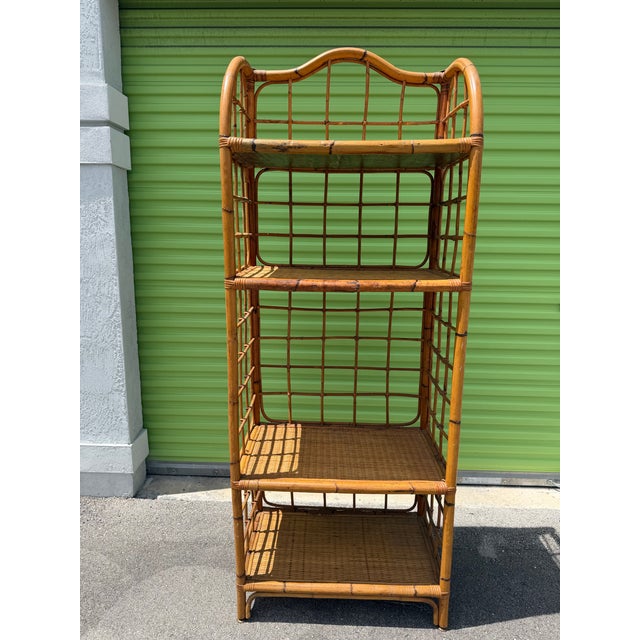 Charming vintage rattan étagère featuring a tall, airy silhouette, gracefully arched top, and four woven cane shelves....