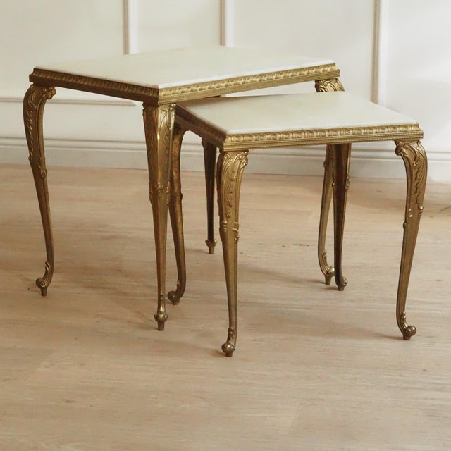 A pair of nesting tables in brass with white marble tops, made around 1950–1960 in the style of Louis XV. The curved lines...