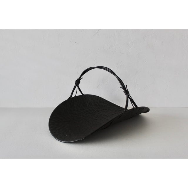 Vintage black metal firewood log holder with a curved, hammered cradle and a wire-wrapped handle. In good vintage...