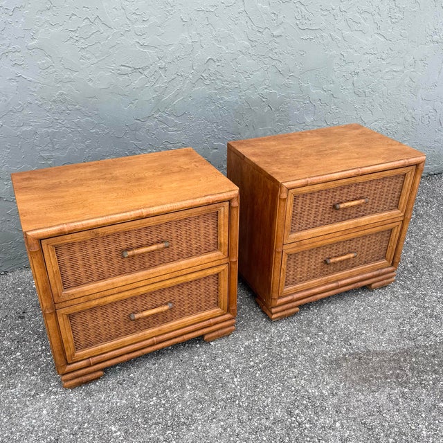 A refined vintage coastal pair of nightstands featuring warm faux bamboo frames and woven wicker drawer fronts. The rich...