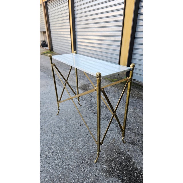 Console table made entirely of brass, supported by X-shaped crosspieces and elegant lion paws. Original marble top nestled...