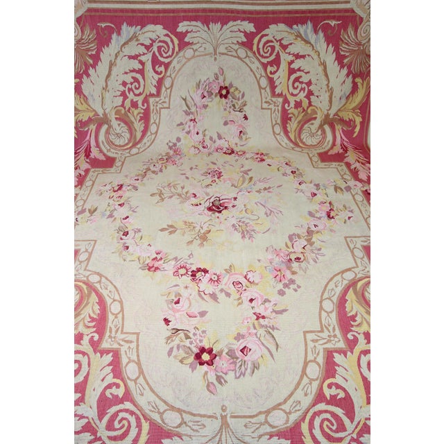 Worked rectangular Aubusson rug with a passively curved cream-colored cartridge on a rose-colored background. The...