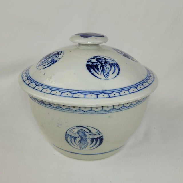 Vintage ceramic lidded bowl features a classic blue and white color palette with intricate crane medallions and geometric...