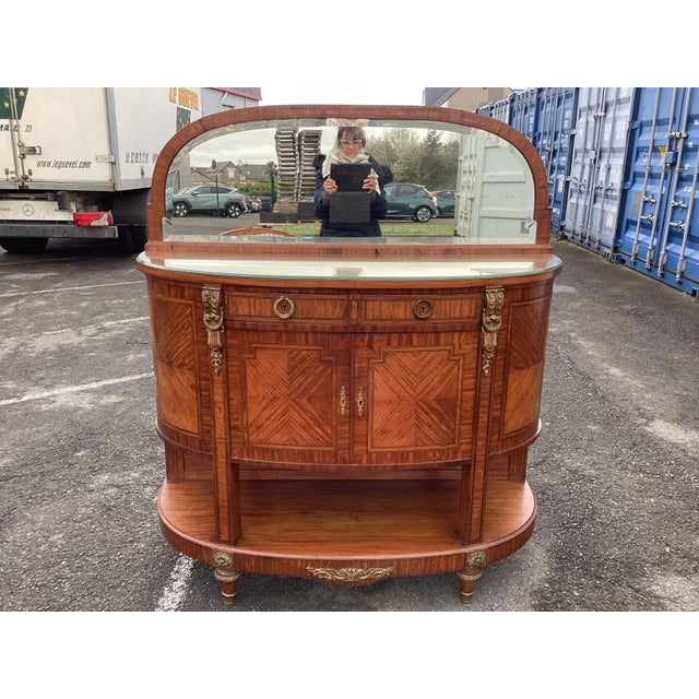 This super elegant French sideboard features straight lines, rounded sides, a bottom shelf, and a large oval mirror. The...