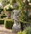 A wonderfully weathered late 20th-century cast concrete garden figure depicting a classical putto carrying abundant...