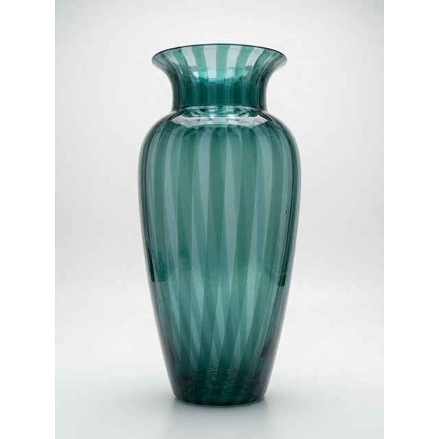 This striking piece features a graceful, elongated amphora form in rich teal-green glass with bold vertical white/clear...