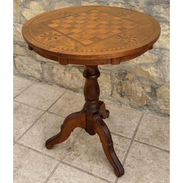 Round games table with marquetry design, string inlay, baluster from pedestal with tripod legs and terminating with a finial.