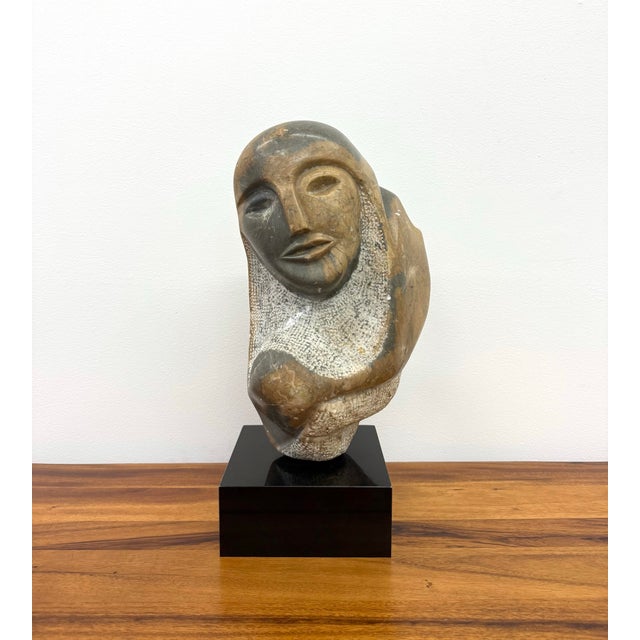 An expressive vintage hand-carved stone sculpture depicting an abstract human bust with stylized facial features and an...