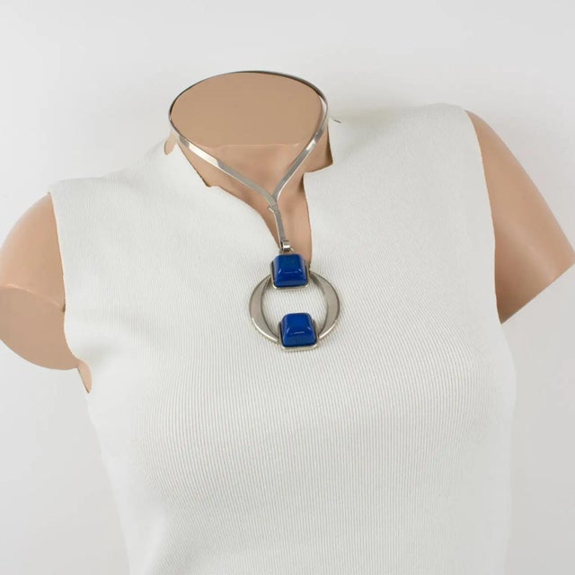 This stylish Mid-Century Modern Space-Age collar necklace has a geometric pendant. The silvered metal rigid neckband is...