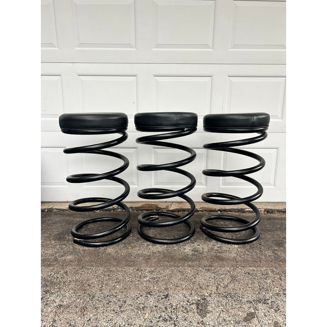 A Set of three "Spring" barstools by Helix co. A soft black vinyl upholstered cushion sits atop a substantial black metal...